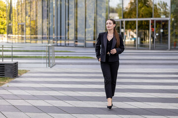 Fototapeta premium Businesswoman walks confidently in front of modern building in urban setting during daylight