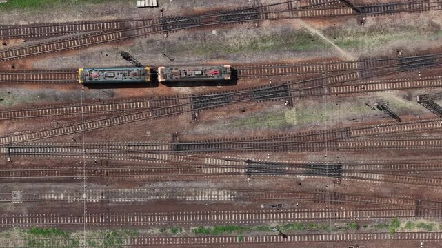 A high-angle aerial view shows two electric train engines sitting on a complex network of railway tracks in Hungary.
