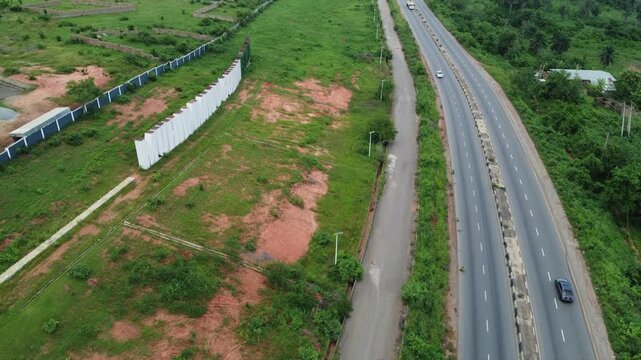 Aerial view of a highway passing through green landscape with red soil patches and a white wall in Abeokuta, Ogun State, Nigeria.