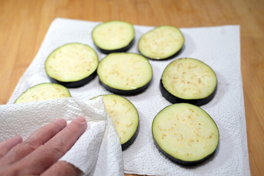 Salted eggplant slices have been sweating and released water, now they being dried with a paper towel before further preparation, cooking theme, selected focus