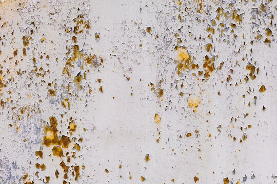 Close-up texture of peeling white paint on metal with yellow-brown rust spots, weathered grunge background.