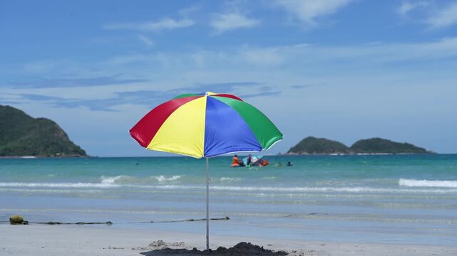 Travel beach umbrella by sea on sand for summer vacation seascape, colorful parasol on quiet shoreline with gentle waves, turquoise water, distant island, bright sky, copy space
