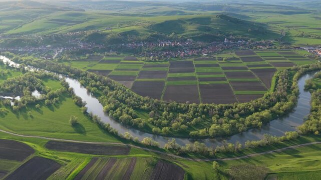 Aerial lateral shot of river curve around rural village and farm fields