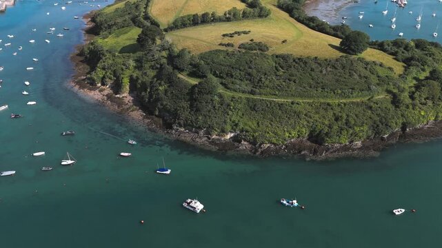 Aerial view of Salcombe Harbour with numerous boats moored in the turquoise waters of the estuary, surrounded by green hills in Salcombe, Devon, United Kingdom.