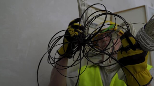 Skilled electrician wearing protective gear handling a messy tangle of electrical cables