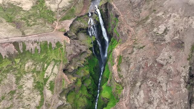 Aerial view of Glymur Waterfall cascading down a deep, mossy canyon surrounded by rugged volcanic terrain and winding hiking trails in Akranes, Akraneskaupstadur, Iceland.