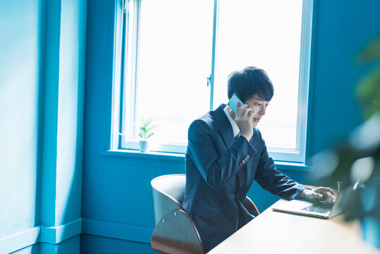 デスクで電話しながらパソコンを使う20代男性ビジネスマン