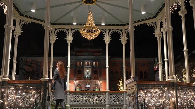Ornate historic gazebo with golden chandelier and Christmas decorations glowing against dark night sky.