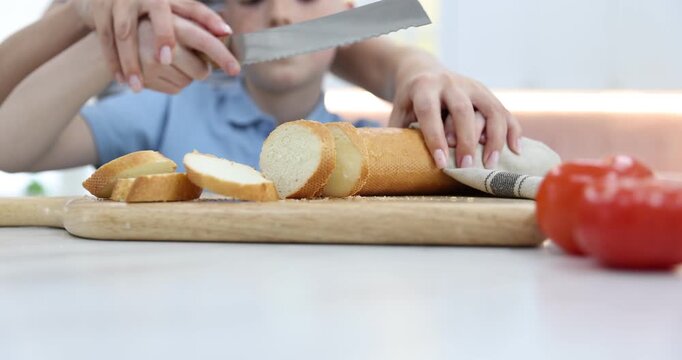 Mother and her son cutting bread together at white table in kitchen, selective focus