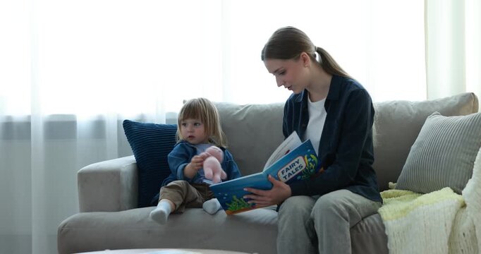 Work for teenagers. Teen nanny reading book to cute baby on sofa at home