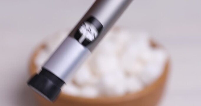 Diabetes. Woman twisting dosage knob on autoinjector pen and putting it onto bowl with sugar at white table, closeup