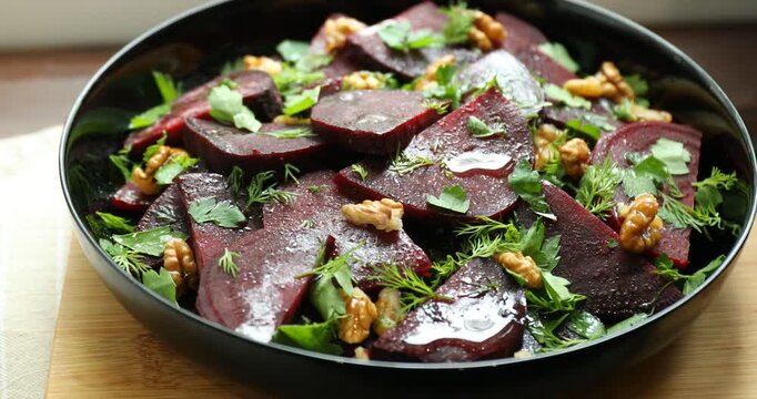 Plate with delicious salad with beetroot, walnuts, dill and parsley turning on table, closeup