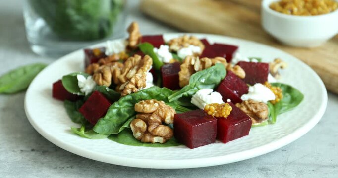 Woman adding walnuts to salad with boiled beets at grey table, closeup