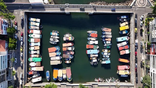 Aerial view of colorful fishing boats moored in the Quadrado da Urca marina, surrounded by urban streets and buildings in Rio de Janeiro, State of Rio de Janeiro, Brazil.