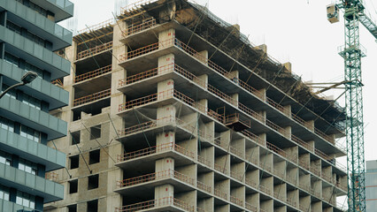 a high rise building is currently under construction, featuring an exposed concrete frame with safety netting and a tower crane nearby © Наталья Добровольска