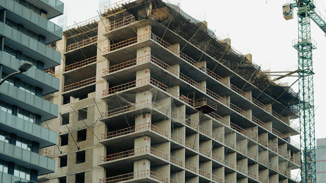 a high rise building is currently under construction, featuring an exposed concrete frame with safety netting and a tower crane nearby