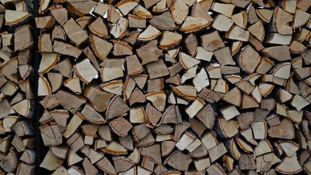 A cinematic close-up shot panning smoothly across a neat stack of chopped birch firewood logs stacked in a woodpile.