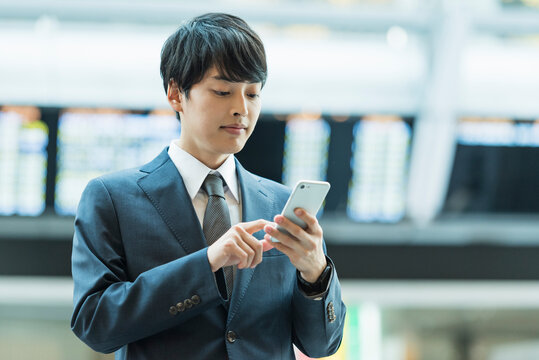 駅のコンコースでスマートフォンを操作する20代男性ビジネスマン