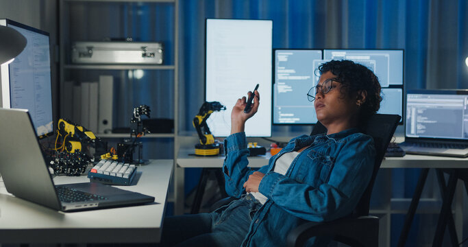 Young African American female programmer coding AI software on multiple screens in night office. Network security, cybersecurity, machine learning, working late, overtime, robotics automation concept.