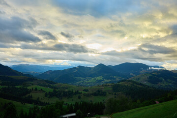 Obraz premium Thick clouds fill the sky over the Carpathian Mountains. Green trees are visible below with fog rolling over the landscape. It appears cold on this cloudy autumn day in Ukraine.