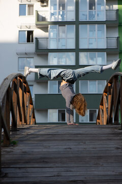 Girl doing handstand split on wooden bridge. Talented preteen girl practicing acrobatic handstand with split legs in an urban residential area. Flexibility, balance and active childhood concept.