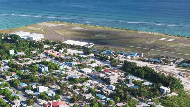 Aerial view of the island town of Kudahuvadhoo featuring residential buildings, lush tropical vegetation, and the adjacent airport runway along the coast in Kudahuvadhoo, Dhaalu Atoll, Maldives.