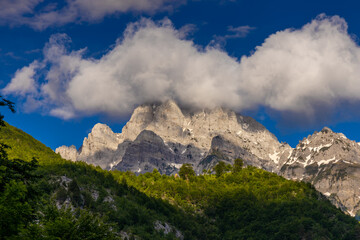 Fototapeta premium Mountain landscape in the Albanian Alps near Theth, Albania. Theth Valbona valley trek Peaks of the Balkans scenic way. Rugged peaks rise above forested valleys and alpine meadows