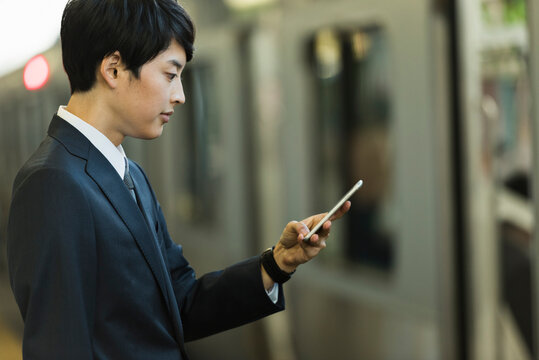 駅のホームでスマートフォンを操作する20代男性ビジネスマン