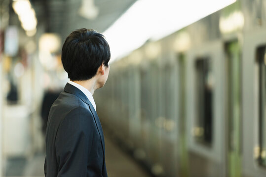 駅のホームで電車を待つビジネスマンの後ろ姿