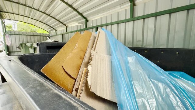 Cardboard boxes and blue plastic rest inside a large dumpster within a covered shelter. This messy pile creates a dreary and overwhelming feeling of endless urban waste.