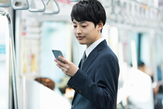電車内でスマートフォンを操作する20代男性ビジネスマン