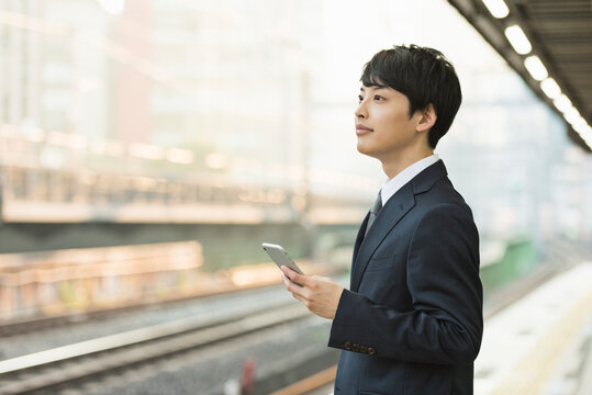 駅のホームでスマートフォンを操作する20代男性ビジネスマン