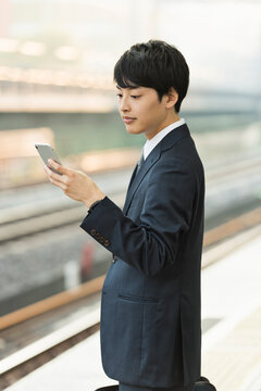 駅のホームでスマートフォンを操作する20代男性ビジネスマン