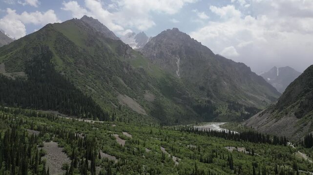 Aerial view of the lush green Ala Archa National Park valley with towering mountain peaks, dense pine forests, and a winding river under a cloudy sky in Bishkek, Bishkek City, Kyrgyzstan.