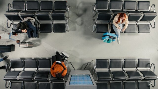 Checking departure board, timetable and top down view of people walking in airport terminal, reading airplane schedule, FIDS display and diverse travelers doing holiday travel, high angle shot.