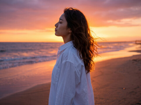 ドラマチックな夕日の海岸で目を閉じる女性