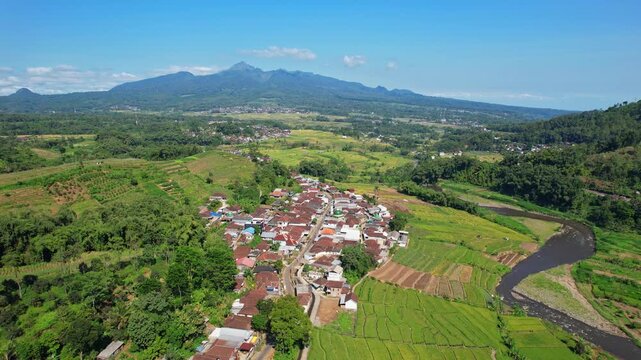 Aerial drone footage of Selorejo valley area, Ngantang, Malang recency, Java island, Indonesia, with many agricultural fields, rice fields and a village, with Kelud volcano mountain behind