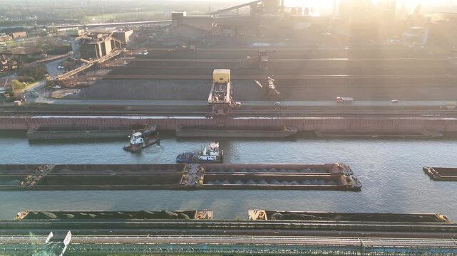 Vertical aerial over port basin showing loaded inland vessel cranes trucks and industrial stockyards
