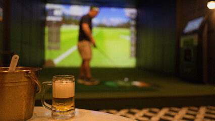 Naklejka premium Cold Beer Mug and Ice Bucket with Blurred Man Playing Indoor Golf