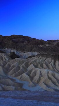 Vertical Screen: Zabriskie Point in Death Valley National Park California displays dramatic eroded mudstone badlands during blue hour with deep shadows accentuating the rippled sedimentary formations.