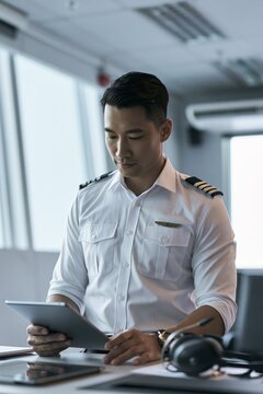 Concentrated pilot of asian descent examining flight plans using a tablet in a contemporary cockpit setting