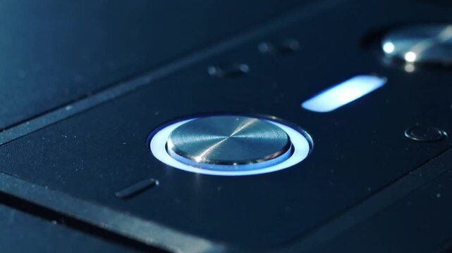 Approaching fingertip pressing metal button on black panel, holding then releasing, activating LED