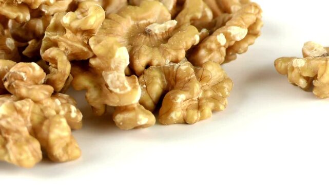 Macro close-up panning shot of shelled raw walnuts scattered on a clean white background