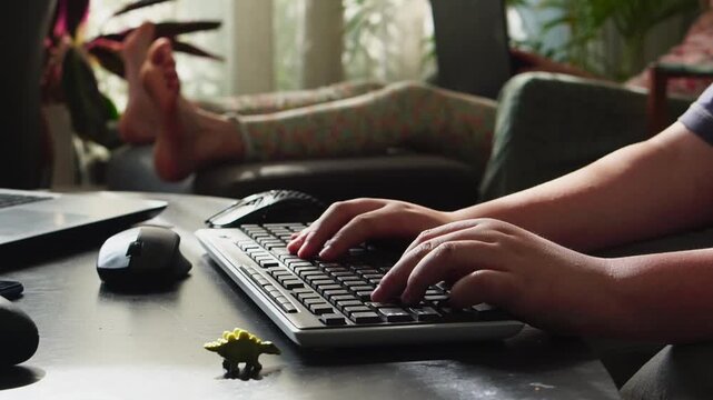 Boy playing computer game using keyboard and mouse, girl with laptop in background moving feet playfully