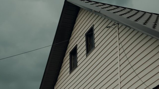 A close-up of the upper floor of a rustic house from the outside, with windows and an attic, electrical wiring, trim, and tiles.