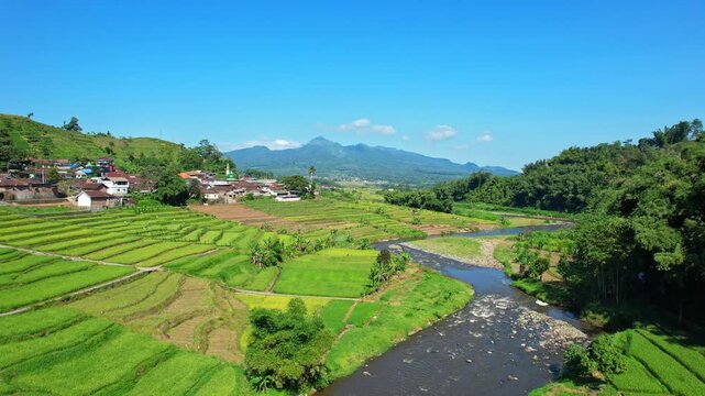 Low aerial drone footage of Selorejo valley area, Ngantang, Malang recency, Java island, Indonesia, with many agricultural fields, rice fields and a village, with Kelud volcano mountain behind
