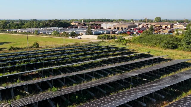 Aerial view of a solar panel field with rows of photovoltaic panels and an industrial railway yard in the background in Saint-Denis-de-l'Hotel, Centre-Val de Loire, France.