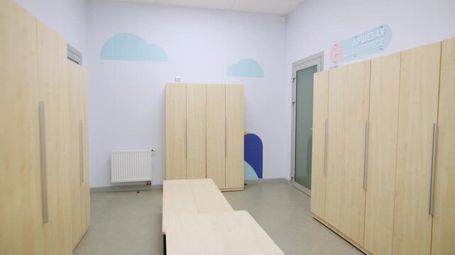 School dressing room displays wooden wardrobes and long changing benches. Cloud illustrations on walls create comfortable surrounding