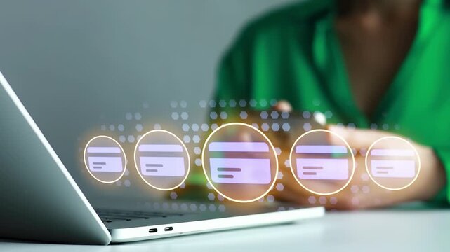 Holding a smartphone while using a laptop with visible digital payment icons during a work session.