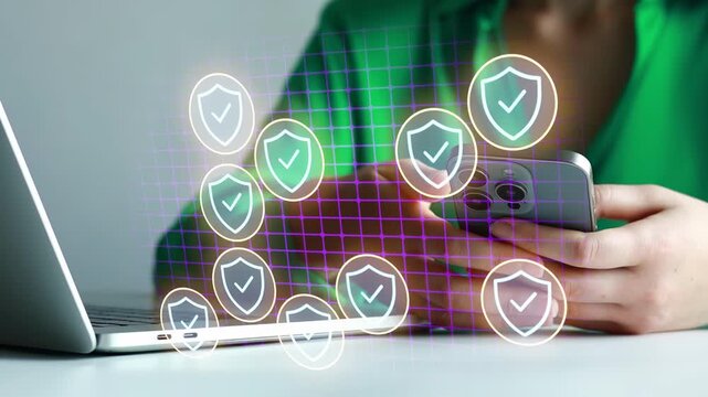 Person using smartphone while sitting at a desk with laptop and security icons in the background.